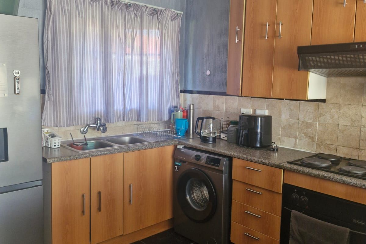 Functional kitchen featuring laminate cabinetry, granite countertops, built-in oven, electric hob, extractor fan, and integrated washing machine with tiled backsplash and flooring.