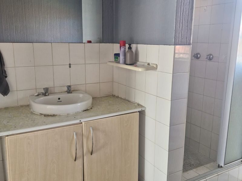 A functional bathroom featuring a vanity cabinet with a basin, a wall-mounted mirror, and a separate shower enclosure with tiled finishes.