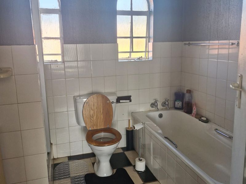 A dated bathroom featuring a standard bathtub, toilet, and tiled finishes with distinctive arched windows.