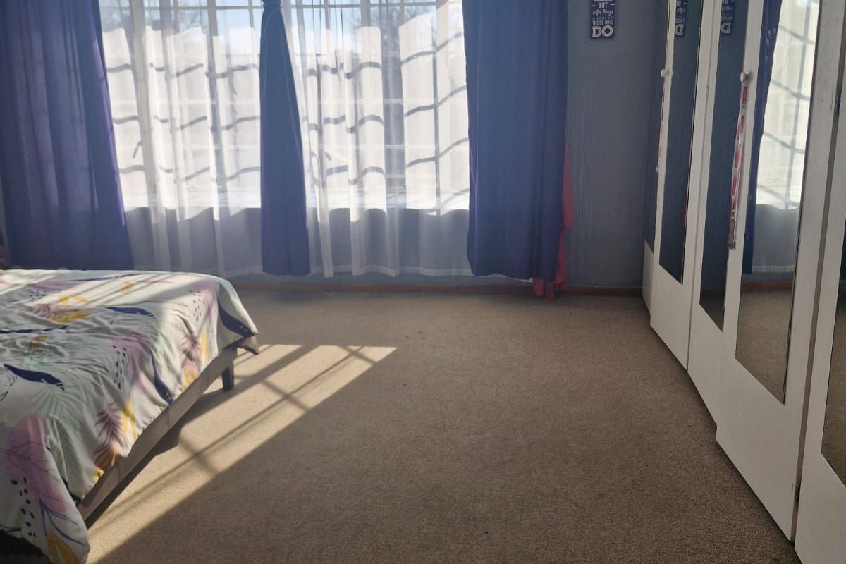 A bedroom featuring carpeted flooring and a wall of built-in cupboards with mirrored doors, providing ample storage space.