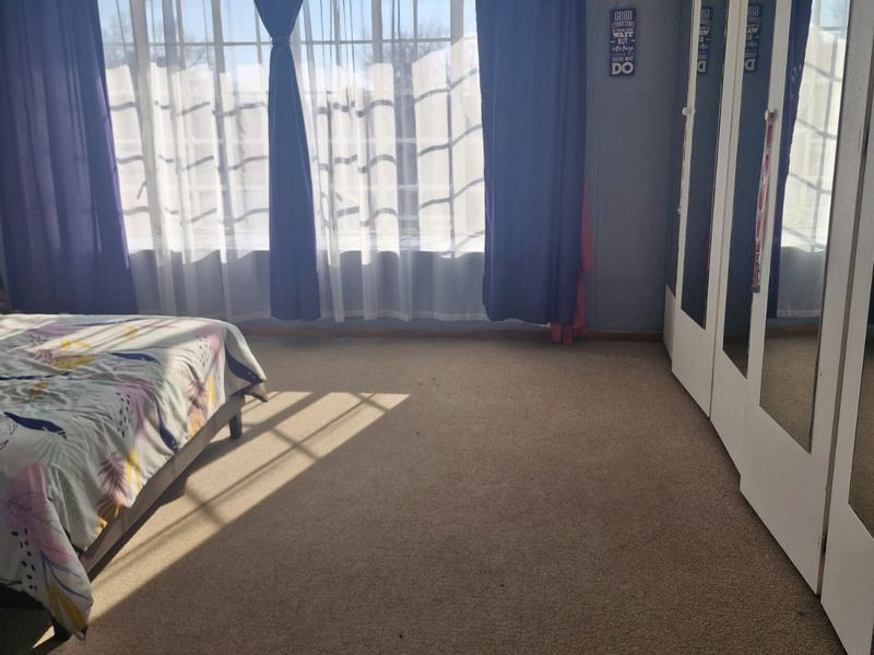 A bedroom featuring carpeted flooring and a wall of built-in cupboards with mirrored doors, providing ample storage space.