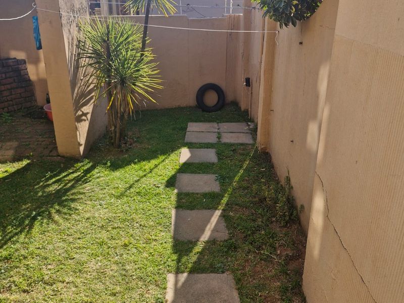 A small rear garden area featuring a lawn, paved walkway, and perimeter boundary walls showing signs of wear.