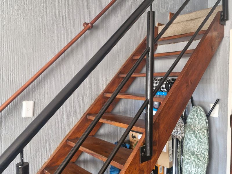 A wooden staircase with a black metal handrail set against a textured grey wall.