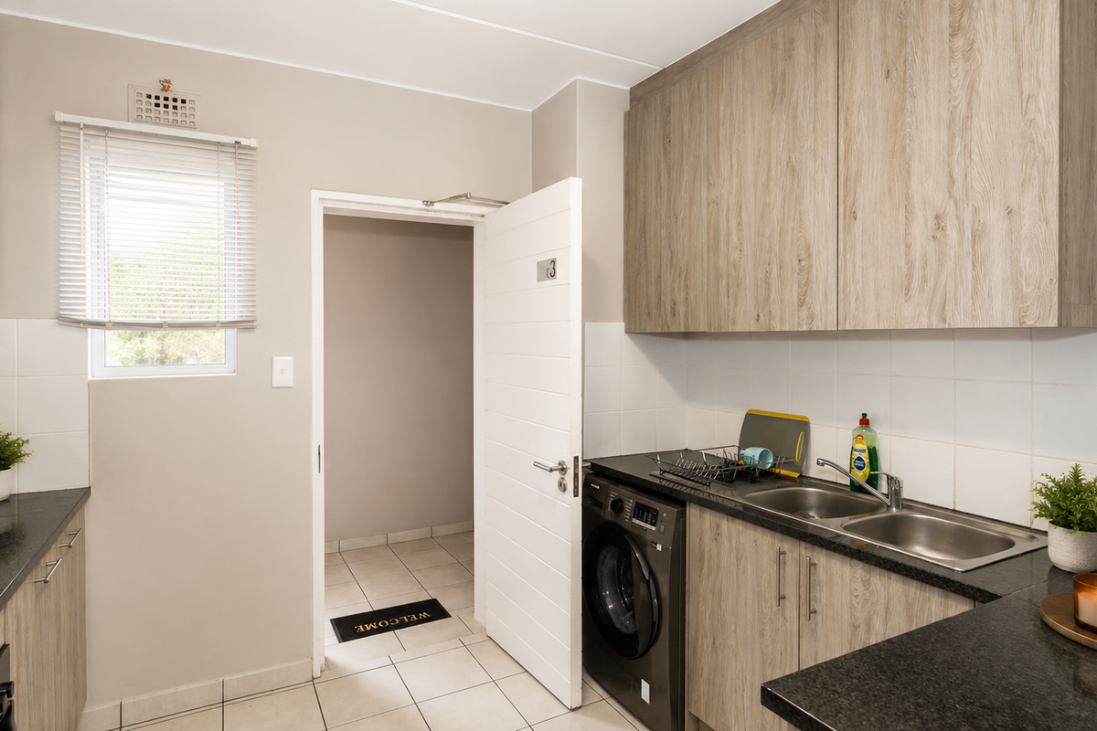 Modern kitchen featuring light wood-grain cabinetry, dark granite countertops, a double stainless steel sink, and integrated space for a washing machine.