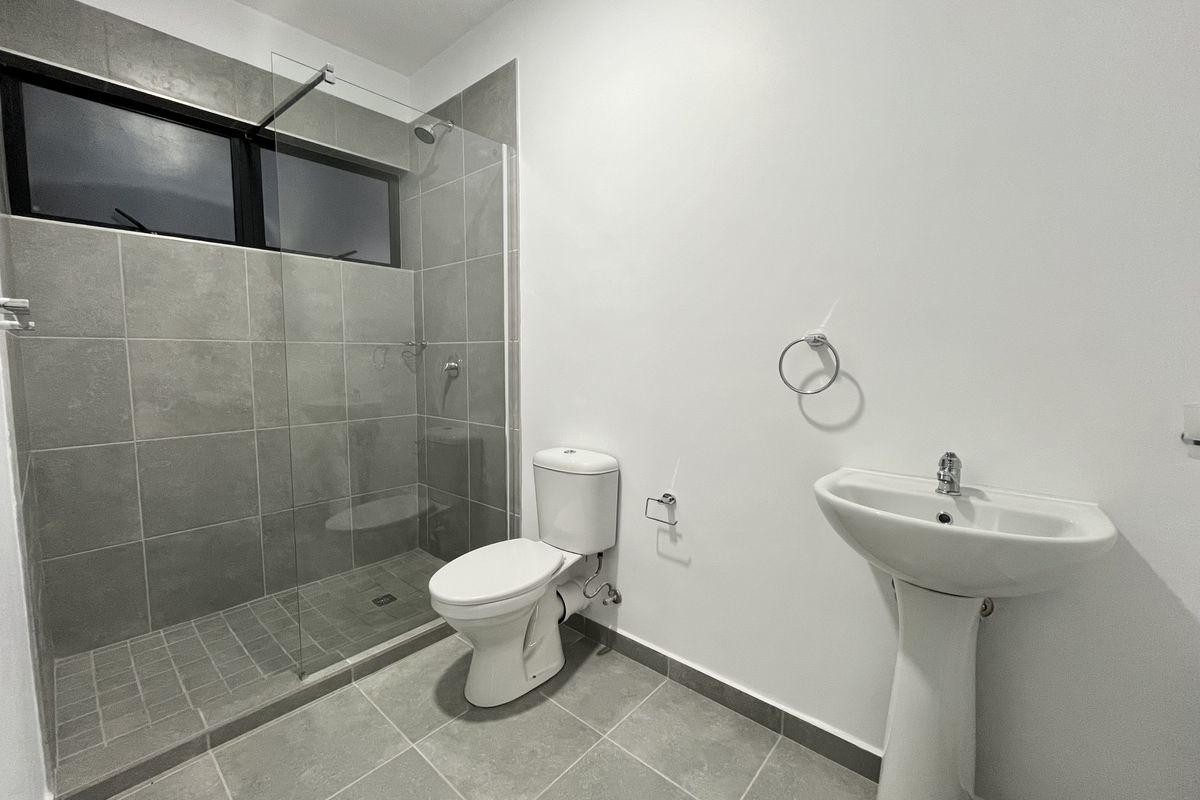 Modern bathroom featuring a glass-enclosed walk-in shower, pedestal sink, and toilet with neutral grey floor and wall tiling.