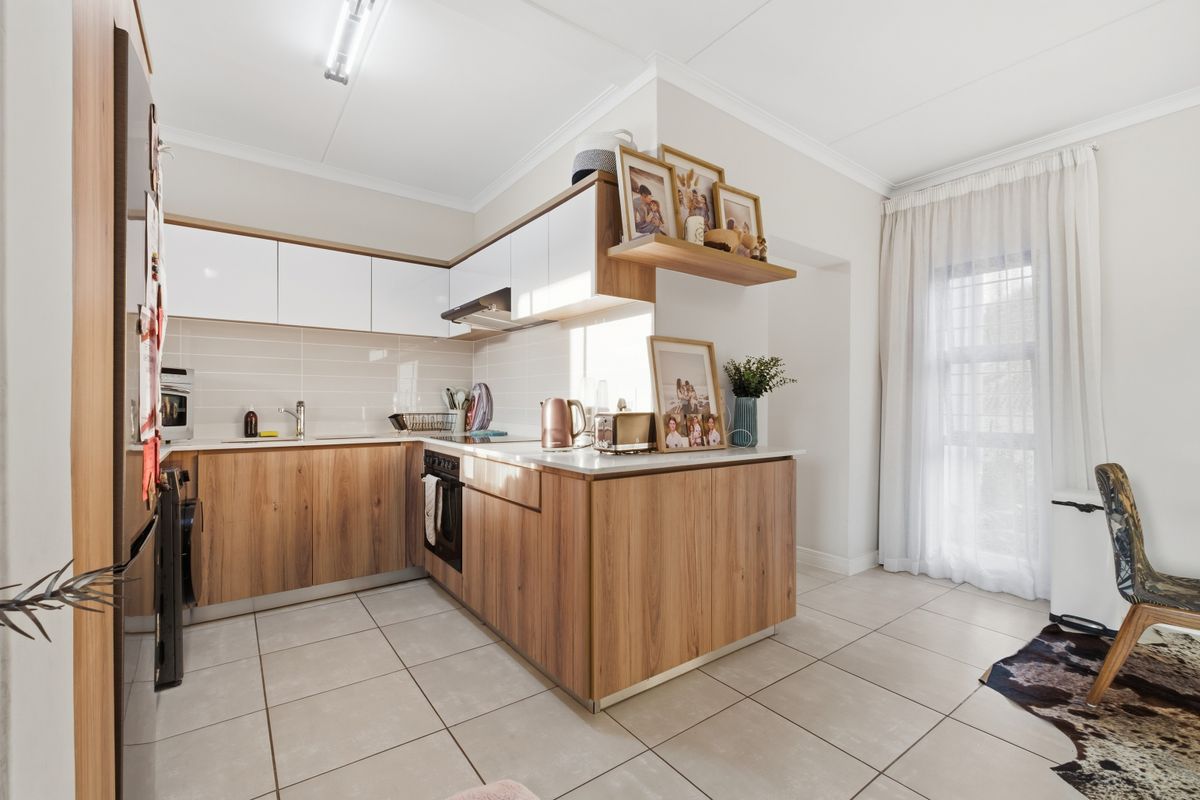 Modern kitchen featuring wood-grain cabinetry, white upper cabinets, integrated oven, extractor fan, and tiled flooring with a bright, open-plan layout.