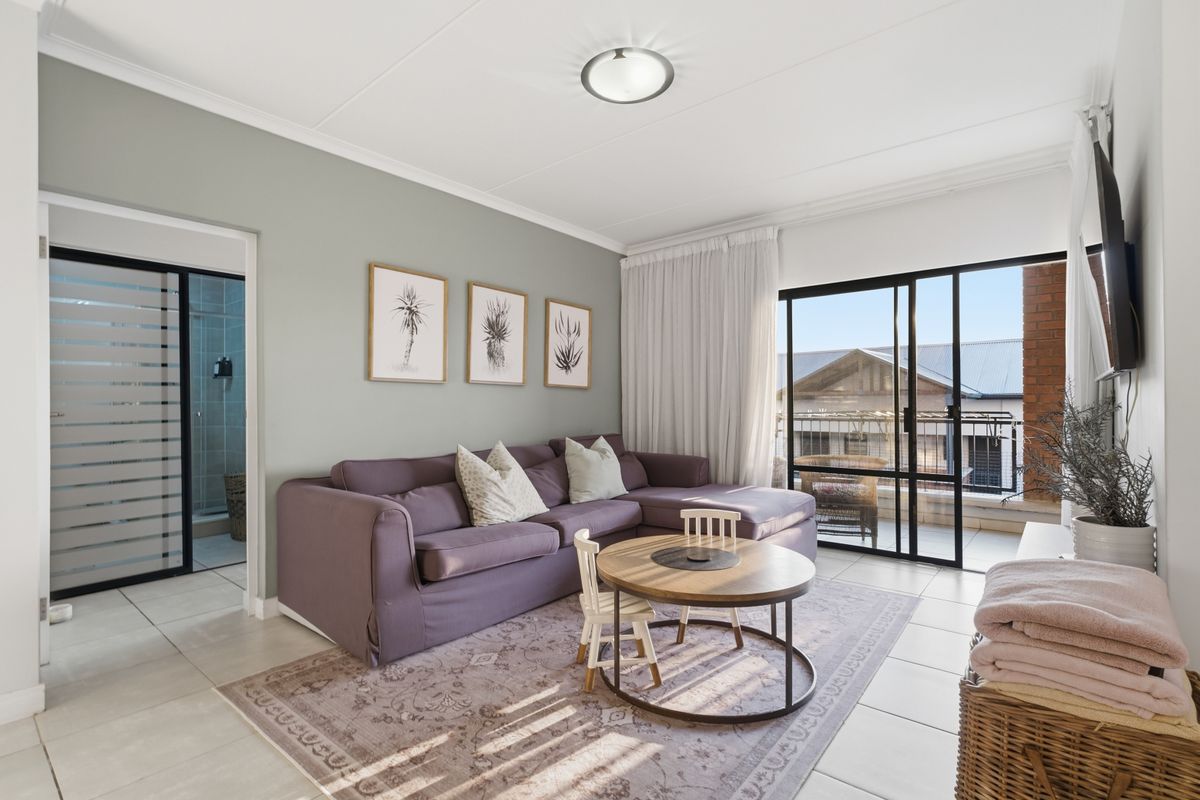 A bright living room featuring tiled flooring, a ceiling-mounted light fixture, and sliding glass doors that open onto a private balcony.