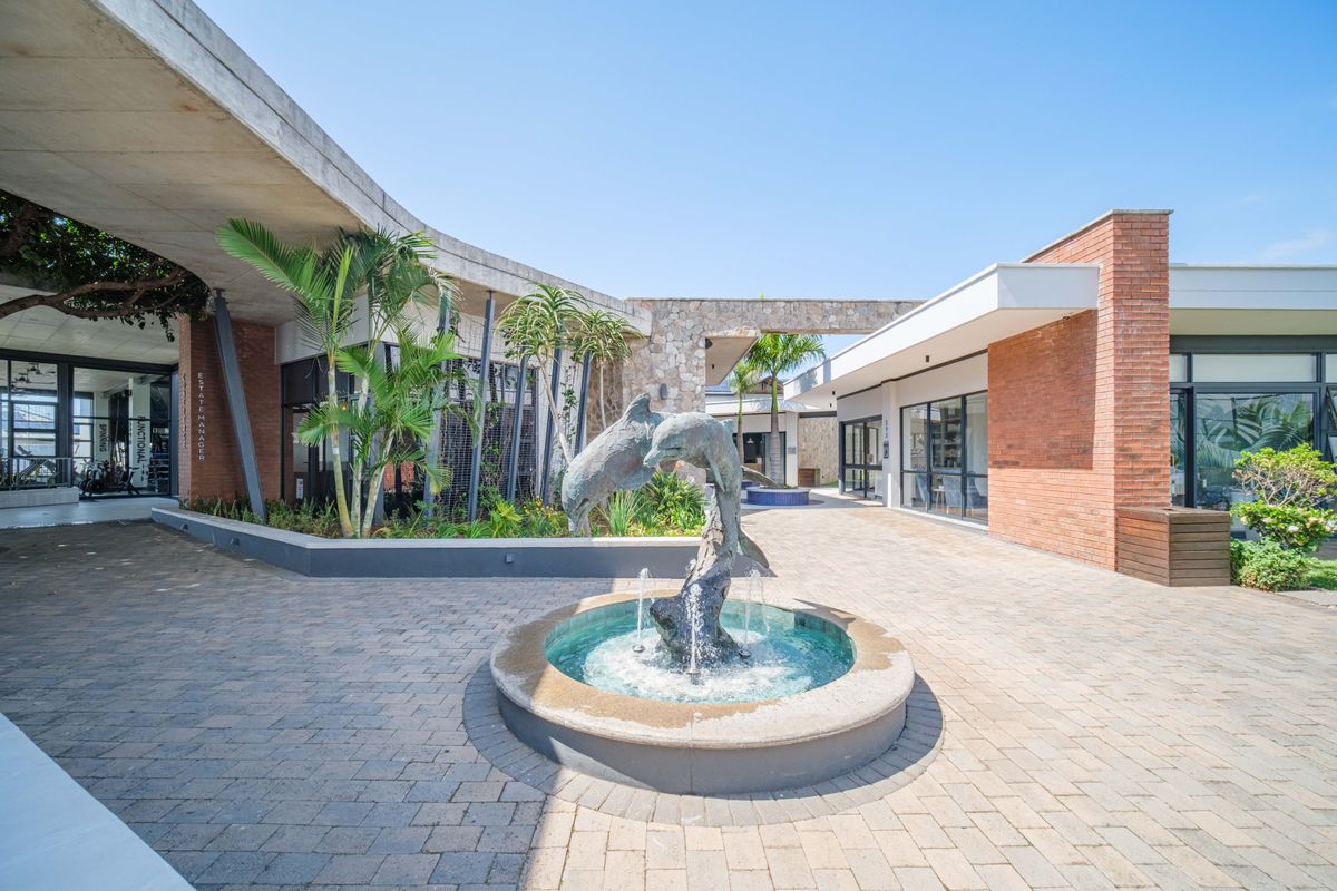 A well-maintained outdoor courtyard featuring a central dolphin fountain, paved walkways, and modern architectural elements connecting the building wings.