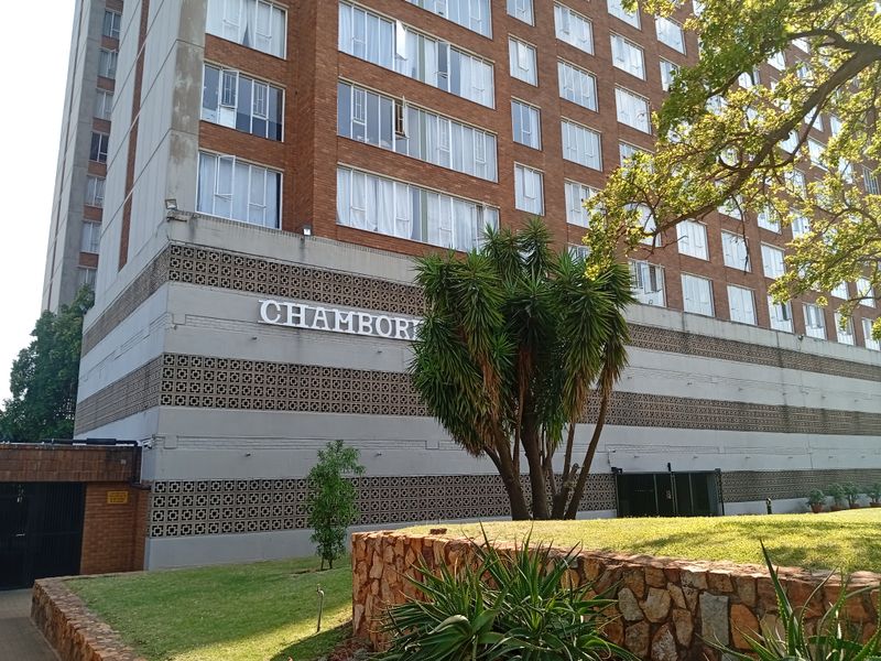 Exterior view of the Chambord apartment building featuring a brick facade, decorative breeze block detailing, and a landscaped garden with stone retaining walls.