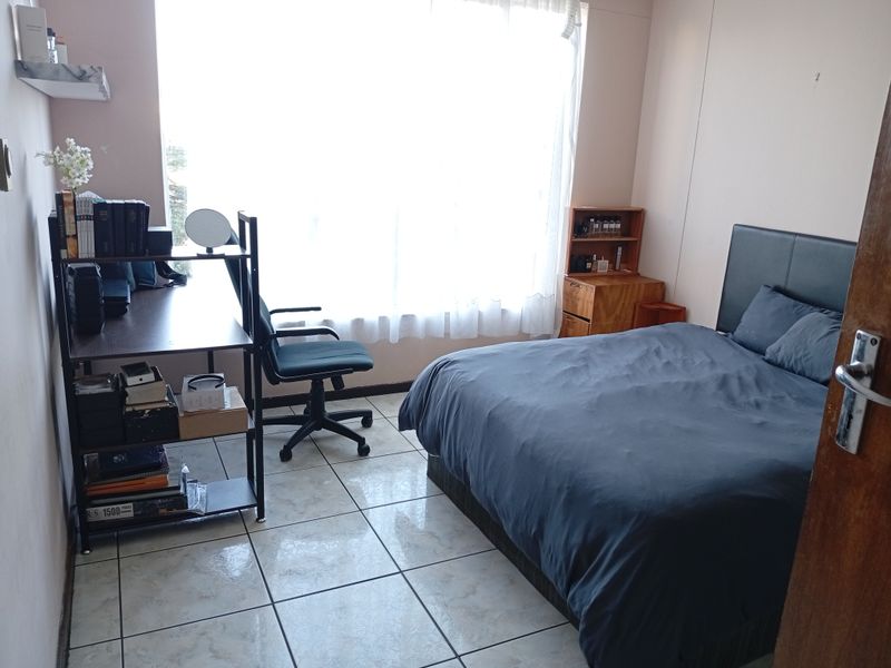 A functional bedroom featuring tiled flooring and a large window that provides ample natural light.