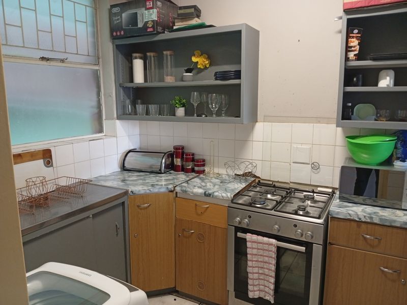 Compact kitchen featuring a gas stove, built-in cabinetry, open shelving, and tiled backsplash, offering a functional layout with potential for cosmetic updates.