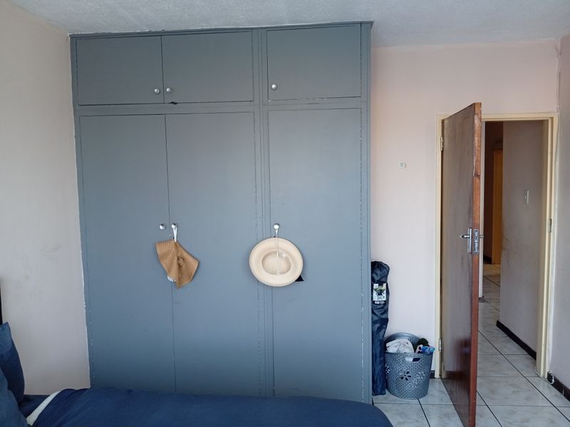 A bedroom featuring built-in grey cupboards and tiled flooring, with an open doorway leading to an adjacent hallway.