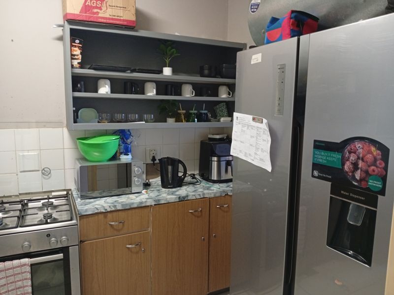 A functional kitchen area featuring a gas stove, oven, laminate countertops, and open shelving with tiled splashback.