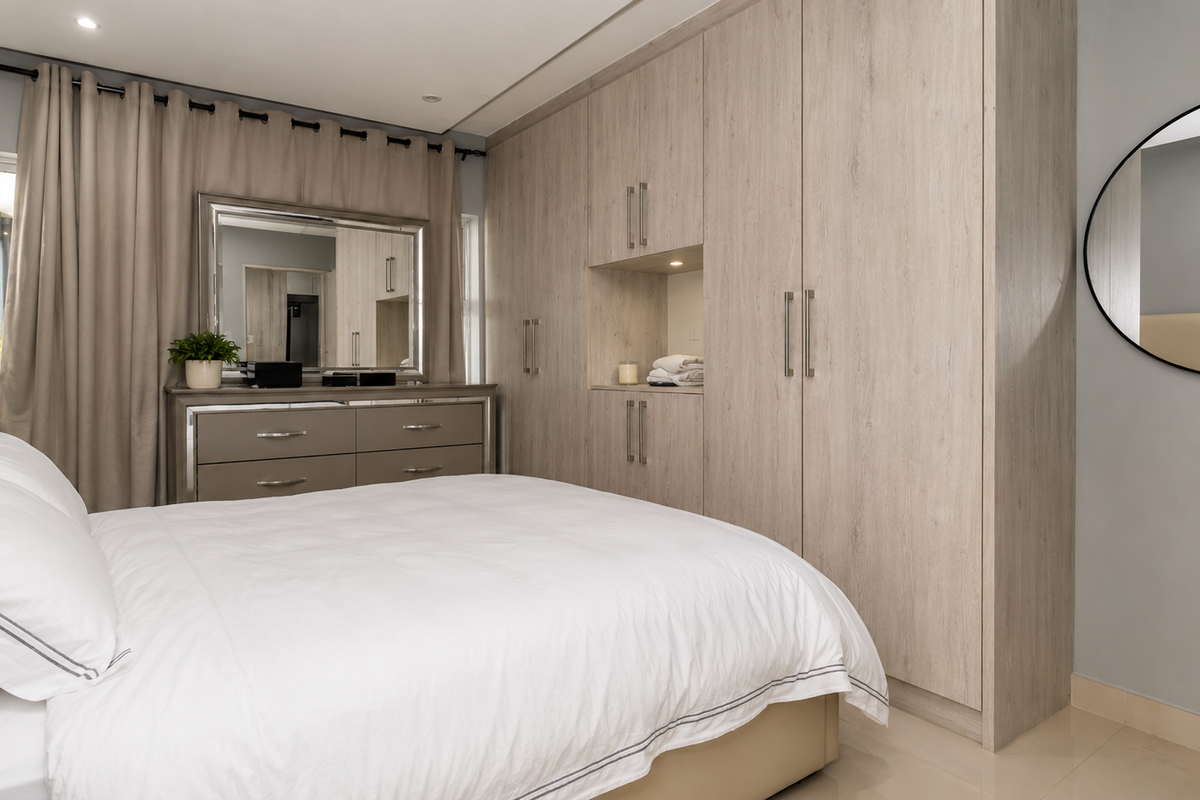 A well-maintained bedroom featuring extensive built-in light wood cabinetry, recessed lighting, and neutral finishes, providing ample storage and a clean, modern aesthetic.