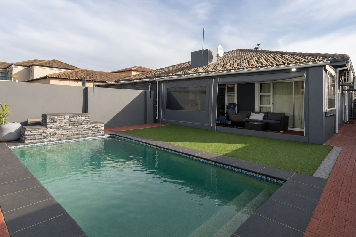 A well-maintained rear garden featuring a swimming pool with stone water feature, artificial lawn, and a covered patio area.