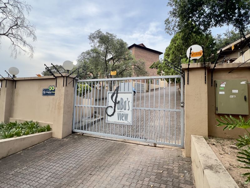 Secure gated entrance to the apartment complex featuring a paved driveway, perimeter wall with electric fencing, and intercom access.