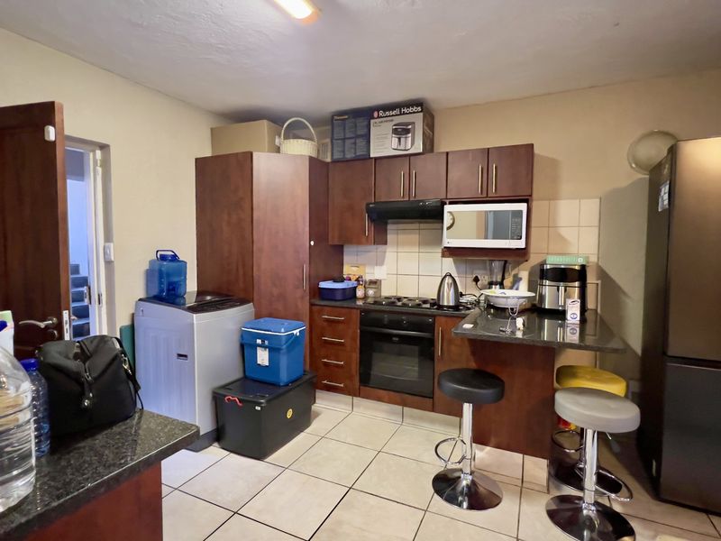 Compact kitchen featuring dark wood cabinetry, granite countertops, integrated appliances, and tiled flooring, offering a functional layout for daily meal preparation.