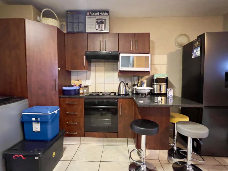 Compact kitchen featuring dark wood cabinetry, built-in oven and hob, tiled backsplash, and a breakfast counter with seating area.