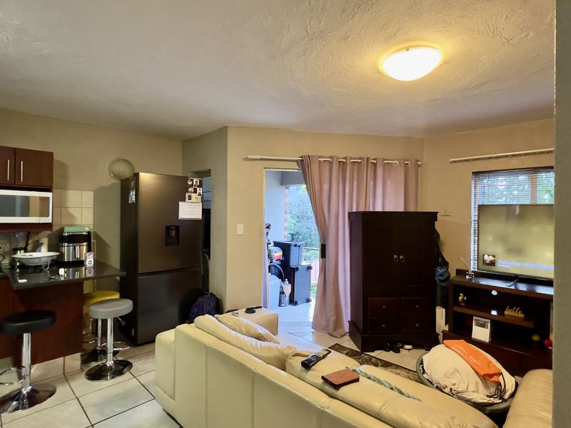 Open-plan living area featuring a compact kitchen with built-in cabinetry and appliances, tiled flooring, and direct access to an outdoor patio area.