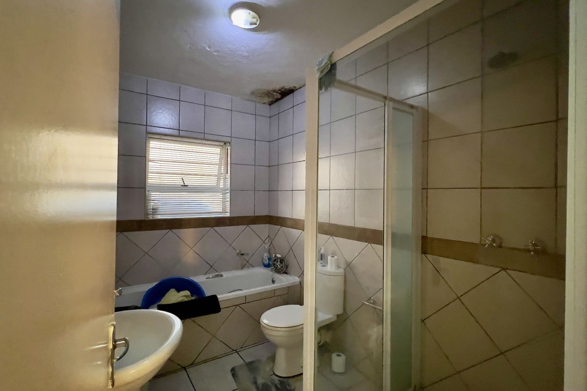 A dated bathroom featuring a bathtub, separate shower enclosure, toilet, and pedestal basin, currently showing signs of ceiling water damage.