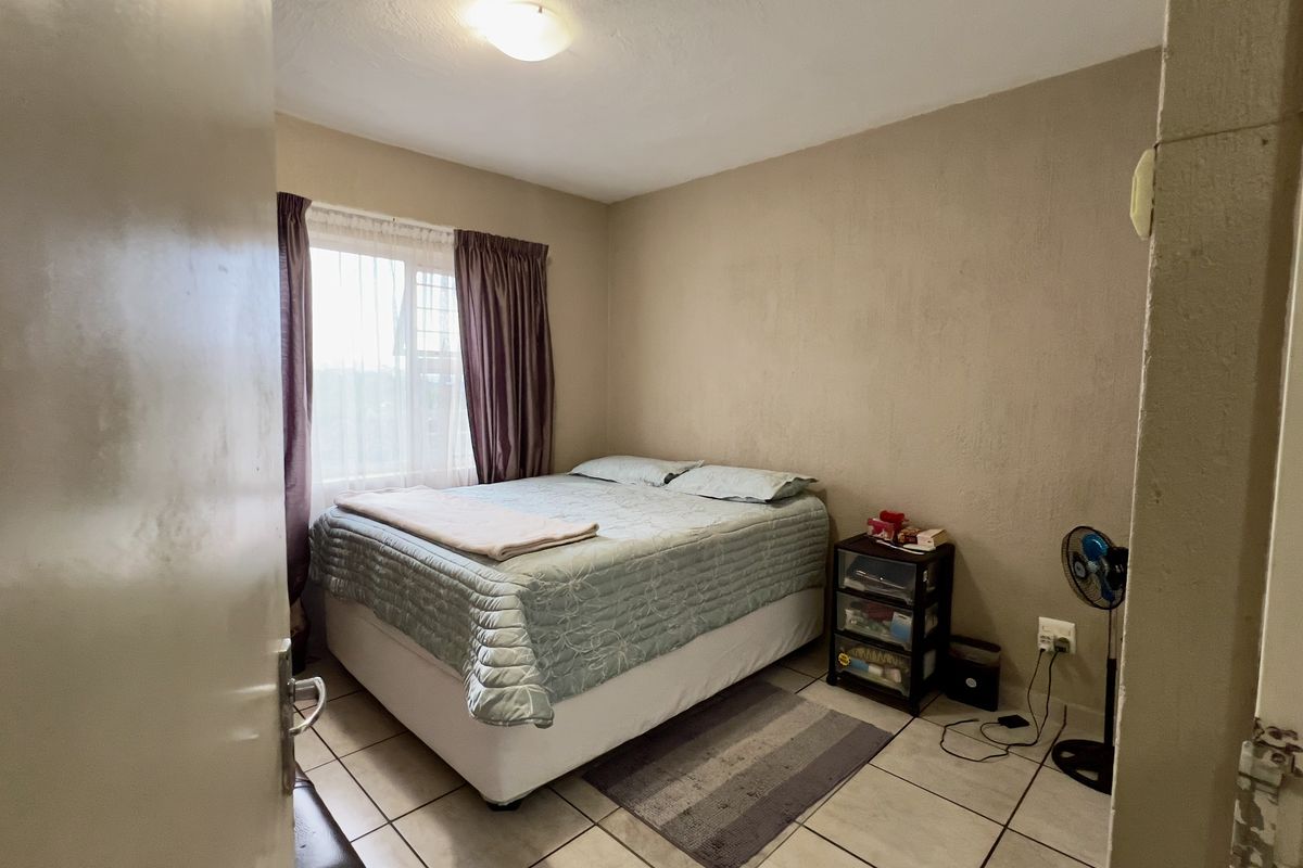 A compact bedroom featuring tiled flooring and a window, currently requiring cosmetic updates to the wall finishes and door frame.