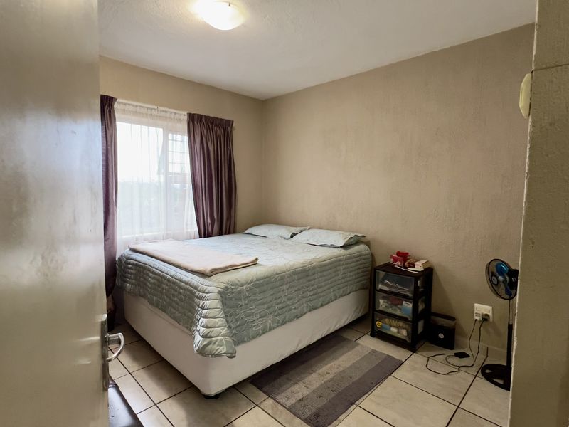 A compact bedroom featuring tiled flooring and a window, currently requiring cosmetic updates to the wall finishes and door frame.