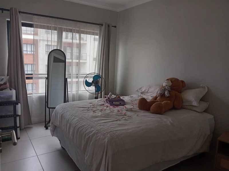 A bedroom featuring tiled flooring and large windows with curtains, providing natural light and a view of the surrounding apartment complex.