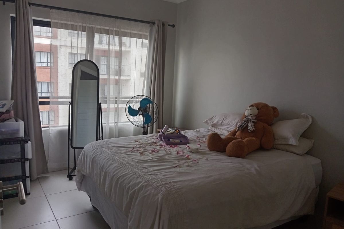 A bedroom featuring tiled flooring and large windows with curtains, providing natural light and a view of the surrounding apartment complex.