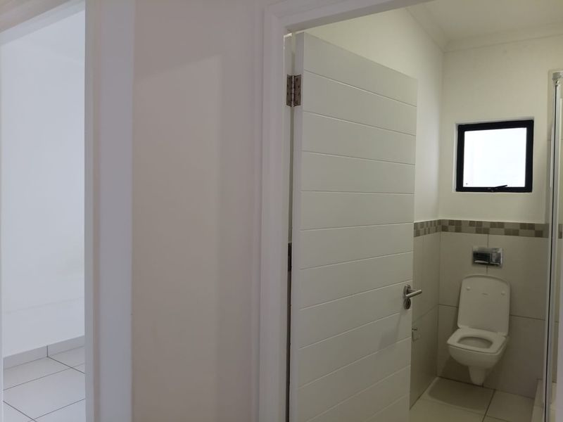 A clean, modern bathroom featuring a wall-mounted toilet, tiled walls with a decorative border, and a window for natural light.