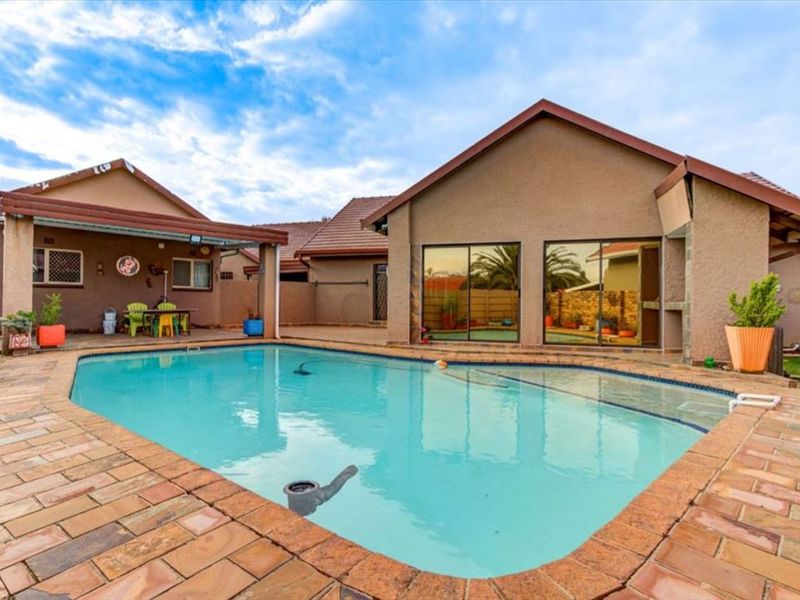 A backyard pool area featuring a swimming pool, brick paving, and a covered patio area with access to the main house via sliding glass doors.
