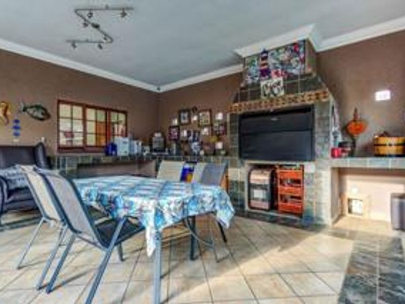 A covered patio area featuring a large built-in braai, tiled flooring, and decorative coving, suitable for outdoor dining and entertainment.