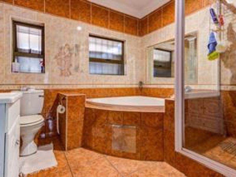 A functional bathroom featuring a corner bathtub, separate shower enclosure, and vanity cabinet, finished with traditional ceramic wall and floor tiling.