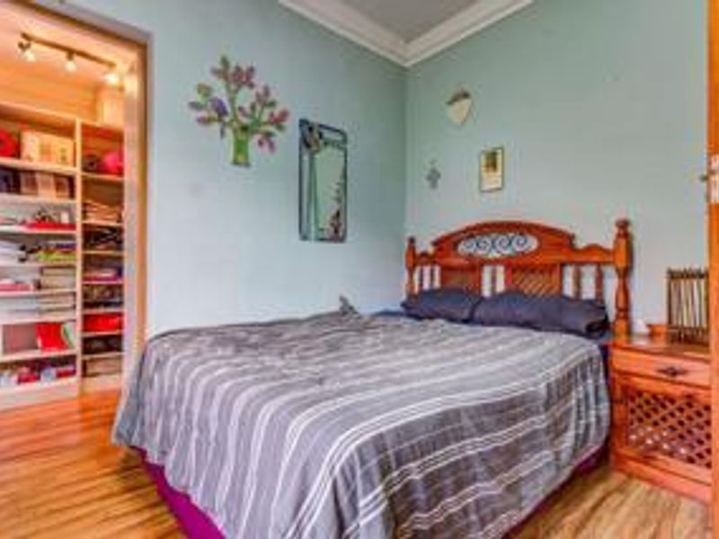 A bedroom featuring hardwood flooring, crown molding, and an integrated walk-in closet with built-in shelving.