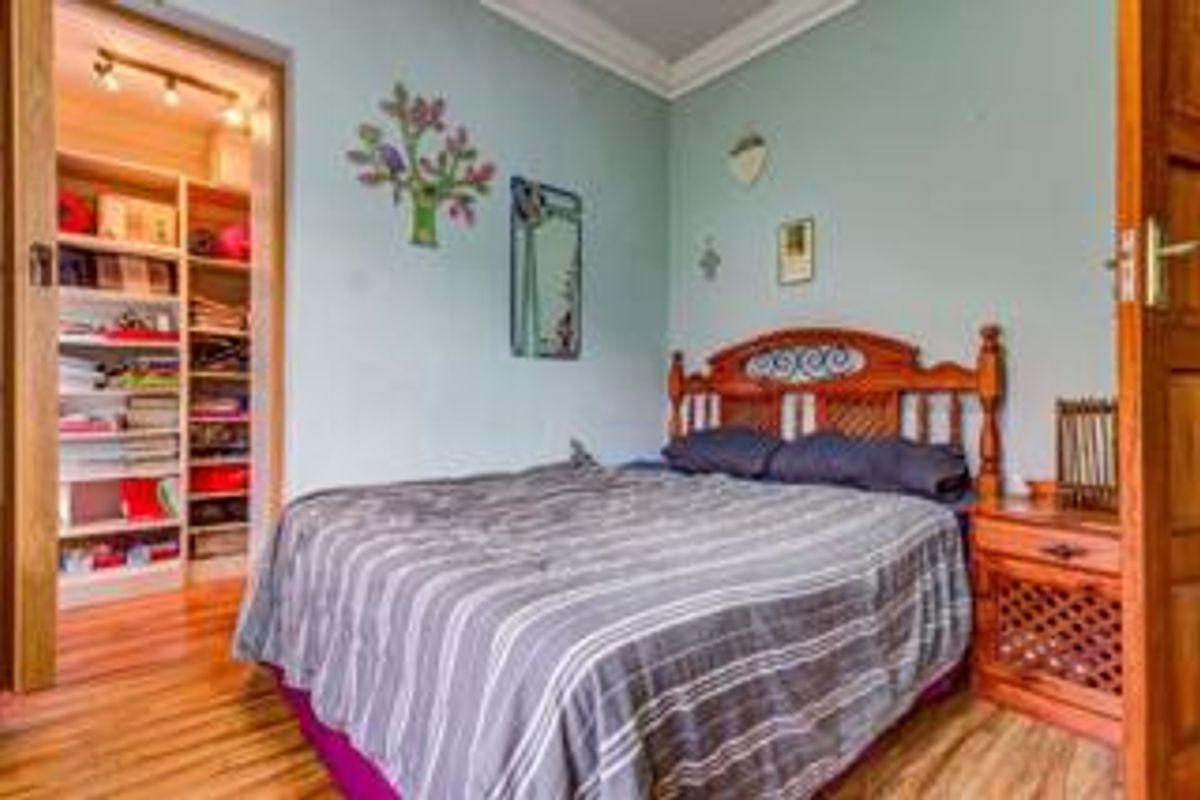 A bedroom featuring hardwood flooring, crown molding, and an integrated walk-in closet with built-in shelving.