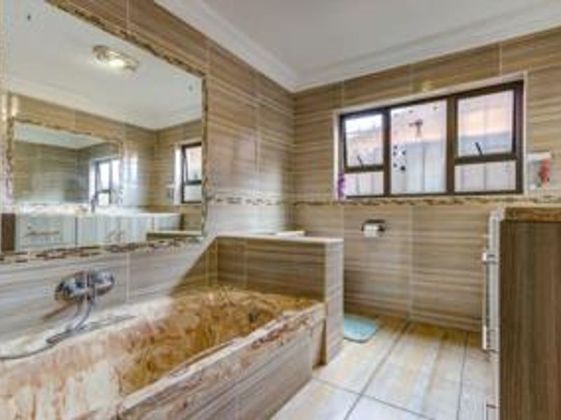 A well-maintained bathroom featuring floor-to-ceiling tiled walls, a built-in bathtub with wall-mounted fixtures, and a large vanity mirror.