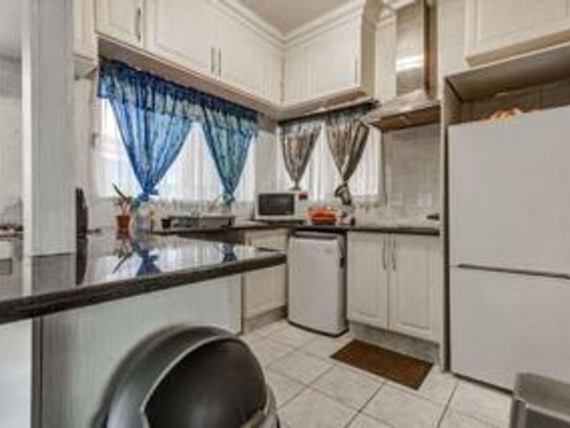 A functional kitchen featuring white built-in cabinetry, granite countertops, a stainless steel extractor fan, and tiled flooring.