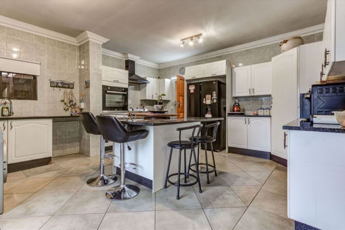 Spacious kitchen featuring white cabinetry, granite countertops, a central island, and tiled finishes throughout.