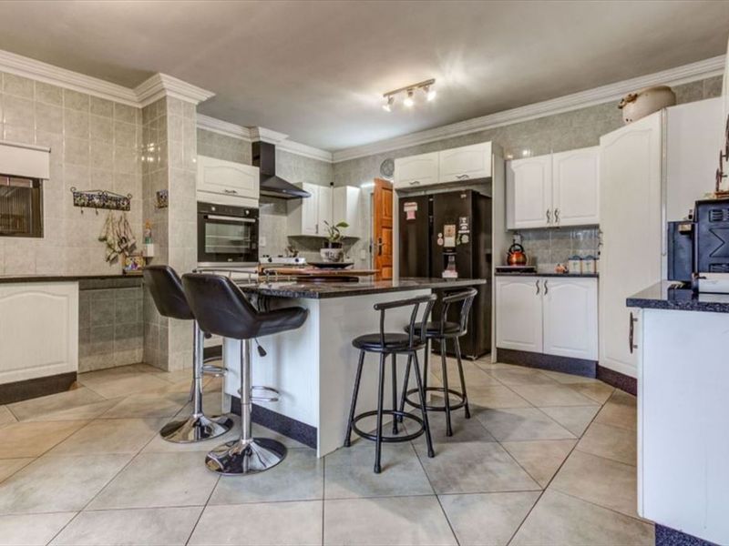 Spacious kitchen featuring white cabinetry, granite countertops, a central island, and tiled finishes throughout.