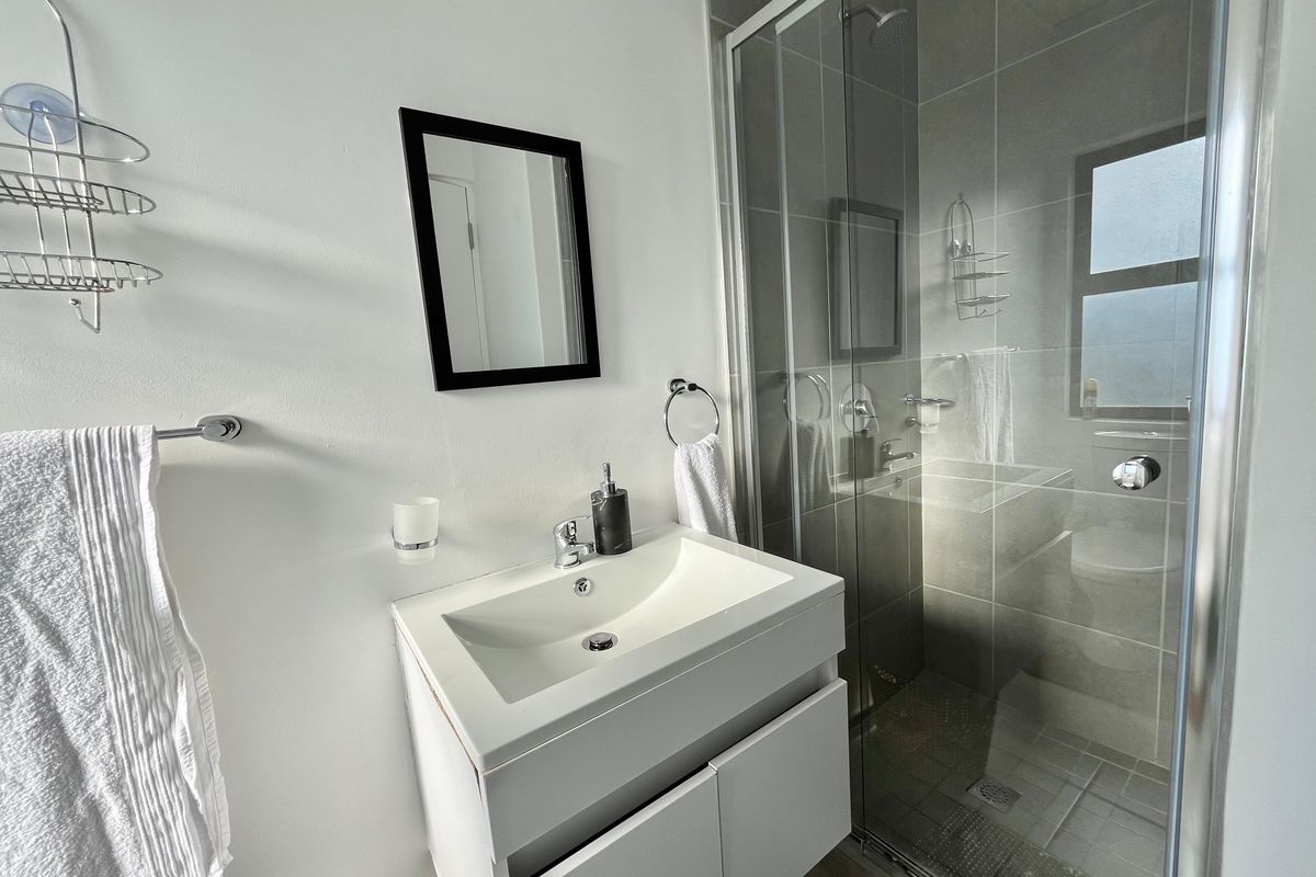 Modern bathroom featuring a white vanity cabinet with integrated basin, chrome fixtures, and a glass-enclosed shower with grey wall tiling.