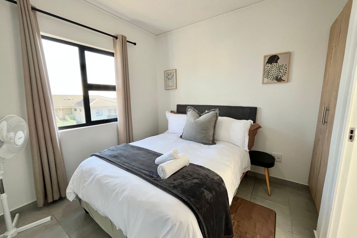 A well-maintained bedroom featuring neutral wall tones, large window for natural light, tiled flooring, and built-in wooden cabinetry.