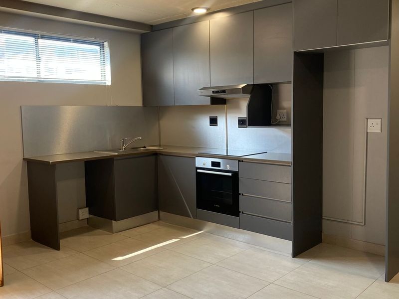 Modern kitchen featuring sleek grey cabinetry, stainless steel backsplash, built-in oven, extractor fan, and tiled flooring in an open-plan layout.