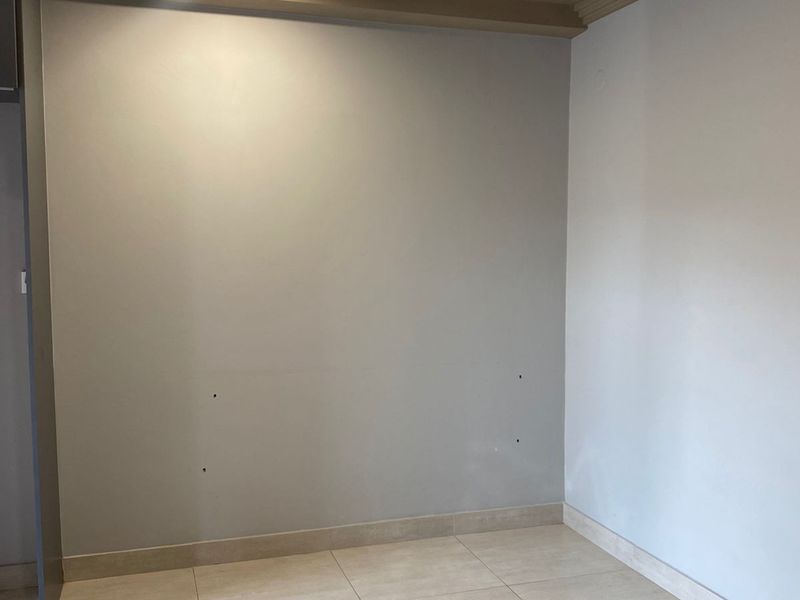 A neutral, empty interior space featuring tiled flooring, recessed ceiling lighting, and clean wall finishes, suitable for various living or office configurations.