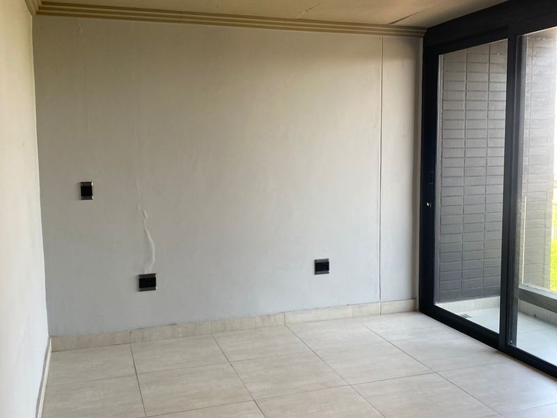 An empty living area featuring large sliding glass doors leading to a balcony, tiled flooring, and recessed ceiling details.