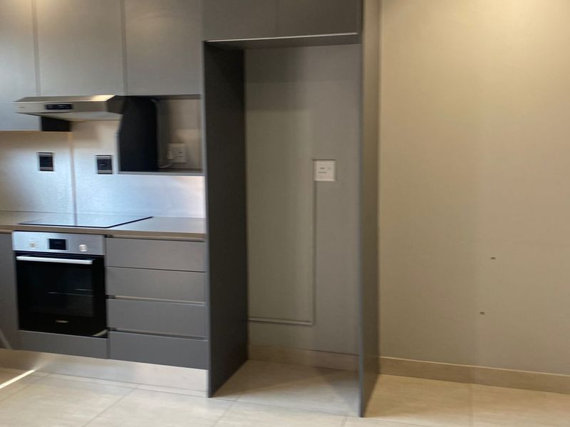 Modern kitchen featuring sleek grey cabinetry, built-in oven, extractor fan, and a dedicated space for a refrigerator.