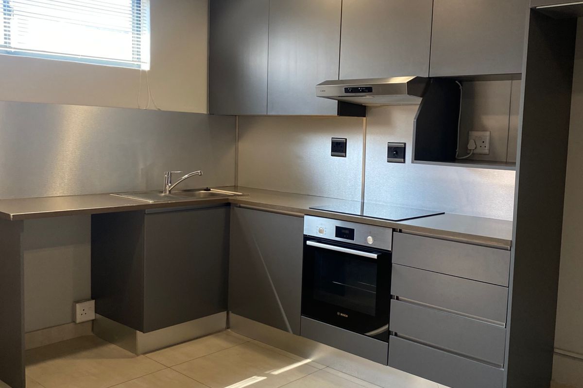 Modern kitchen featuring sleek grey cabinetry, stainless steel splashbacks, built-in oven, electric hob, extractor fan, and tiled flooring.