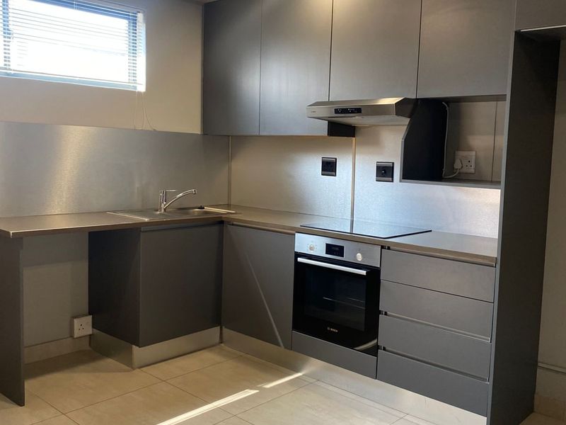 Modern kitchen featuring sleek grey cabinetry, stainless steel splashbacks, built-in oven, electric hob, extractor fan, and tiled flooring.