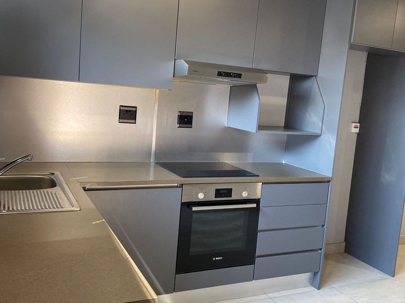 Modern kitchen featuring sleek grey cabinetry, integrated Bosch oven and hob, stainless steel splashback, and neutral floor tiling.