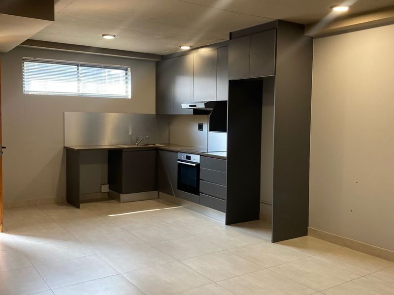 Modern open-plan kitchen featuring sleek dark cabinetry, integrated oven, extractor fan, stainless steel splashback, and neutral floor tiling.