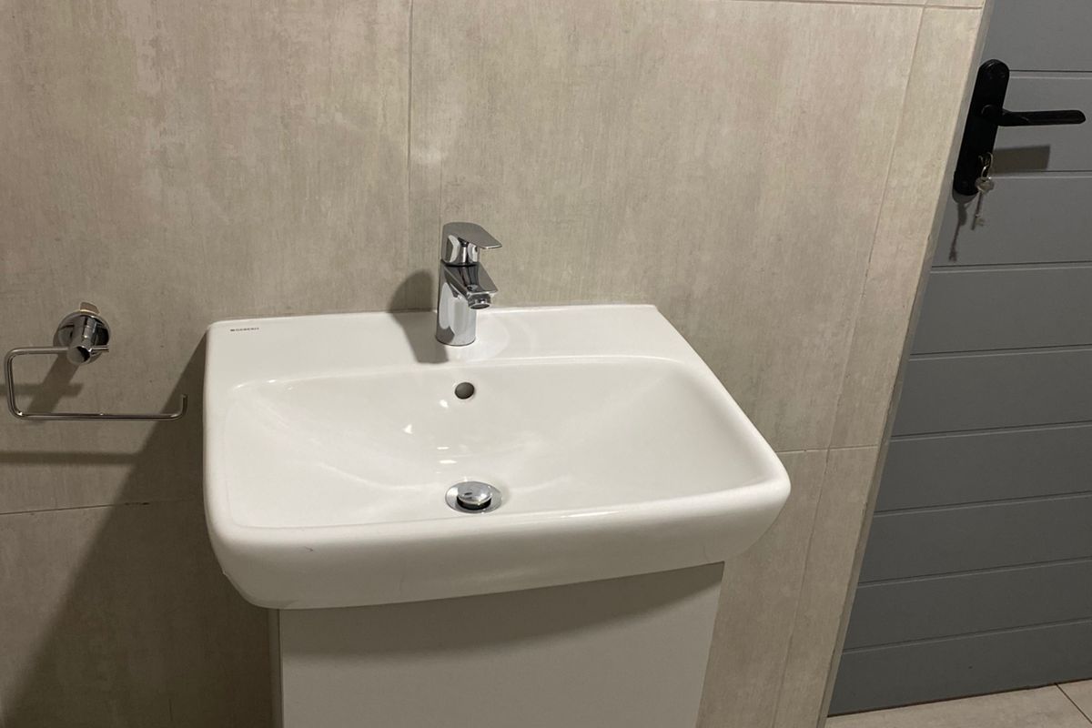 A modern bathroom featuring a wall-mounted vanity basin with a chrome mixer tap and neutral large-format wall and floor tiling.