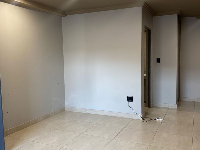 An empty living area featuring neutral tiled flooring, recessed ceiling lighting, and a clean, minimalist aesthetic ready for personalization.